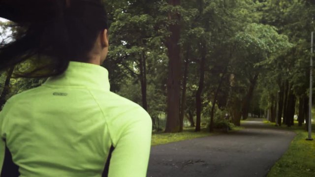Young sexy runner brunnete woman with good shapes in green blouse running in park. Portrait super slow motion shot back spine back.