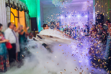 Beautiful caucasian couple just married and dancing their first dance confetti and heavy smoke around. Bride and groom kiss.