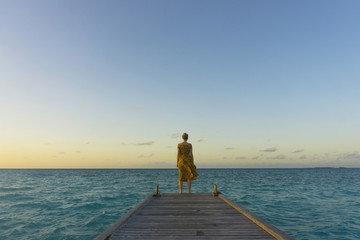 Female traveller at the end of a wooden pier at sunset
