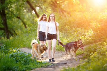 Two smiling teenage girls walking with her dogs in spring park. Friendship concept background