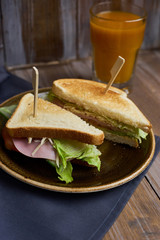 Club sandwich with cheese, ham, lettuce and toast bread on plate and glass of Sea-buckthorn berries juice on wooden table