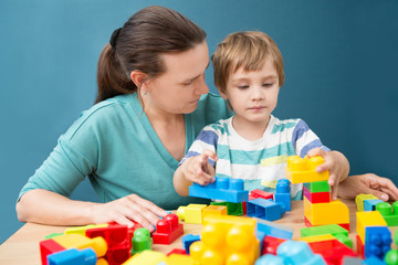 mother and little son  playing with lots of colorful plastic blocks constructor indoor.  The happy family spends time together at home.