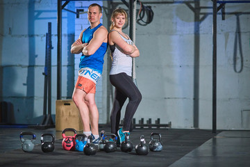 Sporty man and young muscular woman doing an exercise with weights in the gym