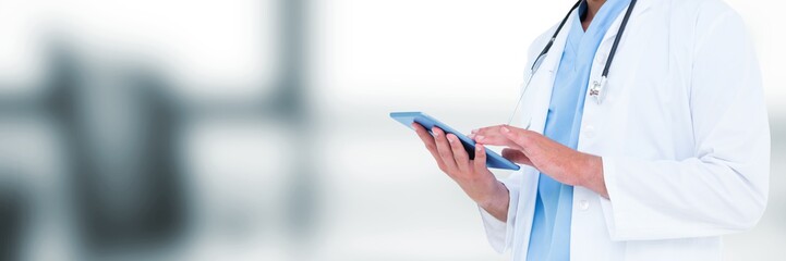Doctor mid section holding tablet against blurry grey office