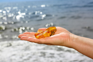 Three transparent polished piece of amber on the palm on the background of the sea. The hand holds the amber pieces on the beach. A natural mineral made from resin trees. Ancient mineral. Sunstone 