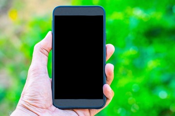 Male hand holding a smartphone on a tree bokeh background using a wallpaper or background for communication  work.