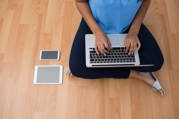 Female executive using laptop while sitting on wooden floor