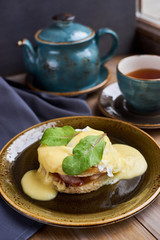 Breakfast. Delicious eggs benedict served on plate. Teapot and cup of hot black tea.