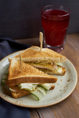 Club sandwich with cheese, ham, lettuce and cucumber with toasted bread on plate and glass of cranberry juice