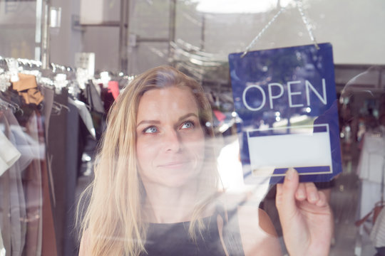 Pretty blond woman turning the open and closed sign in clothes shop
