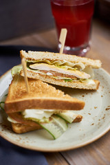 Club sandwich with cheese, ham, lettuce and cucumber with toasted bread on plate and glass of cranberry juice