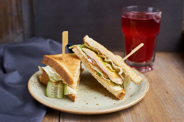 Two Club sandwich with cheese, ham, lettuce and cucumber on plate and glass of cranberry juice on wooden table