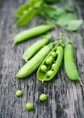 Pods of green peas on a old wooden surface close up, soft focus