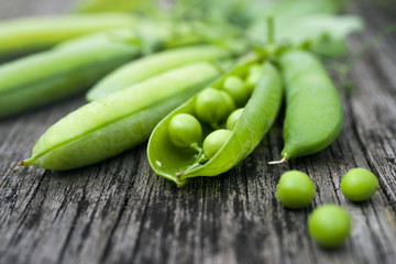 Pods of green peas on a old wooden surface close up, soft focus