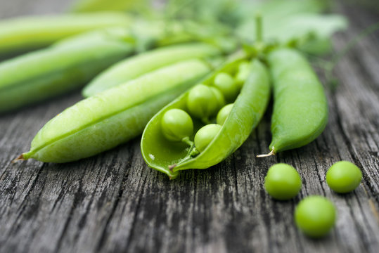 Pods of green peas on a old wooden surface close up, soft focus
