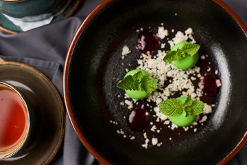Delicious caramelized apples dessert with mint flowers at big black plate with hot black tea. Top view.