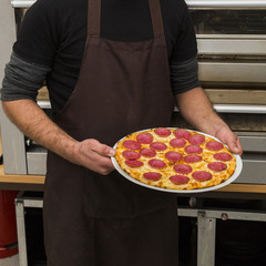 Chef holds plate with hot freshly prepared salami pizza.
