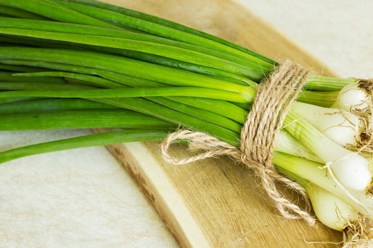 Spring green onion on a wooden board. Light background. Country style. Selective focus. Close-up.