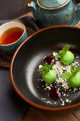 Delicious restaurant dessert from apples, chocolate, mint and caramel glazed in form of small apples with leafs. Dessert from chef. Served with teapot and cup of hot black tea.