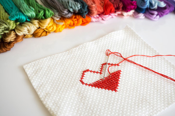 Stitching red heart shape on white fabric on white background.