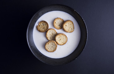 Danish koldskaal - cold buttermilk soup with crispy biscuits named kammerjunker served in rustic black bowl, isolated on black background