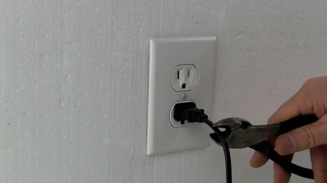 A man cuts electric AC power cord plugged into wall outlet with wire cutters 