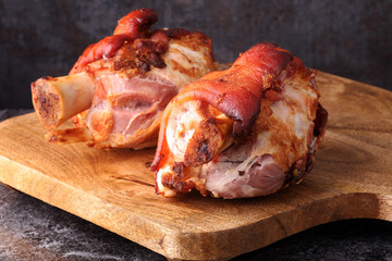 Smoked ham hock with herbs and spices on wooden plate.