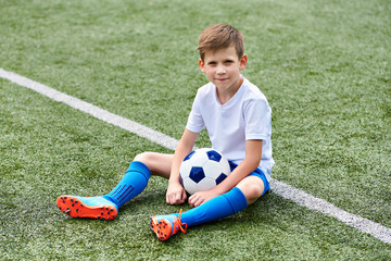 Fototapeta premium Boy football soccer with ball sitting on grass