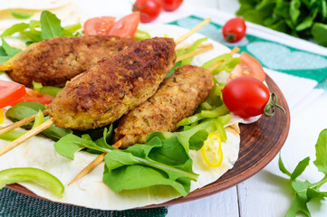 Minced meat on skewers - lula kebabs on a plate with fresh vegetables and greens on a white background. Top view. A traditional Central Asian dish.