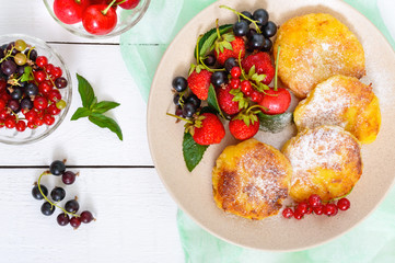 Golden cottage cheese pancakes with fresh berries on a plate on white wooden background. Top view. Proper nutrition.