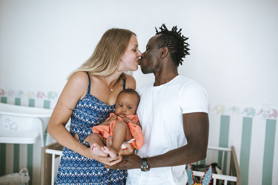 multicultural parents kissing and holding their child