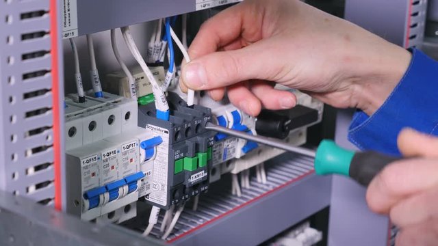 Worker using screwdriver on electrical equipment.