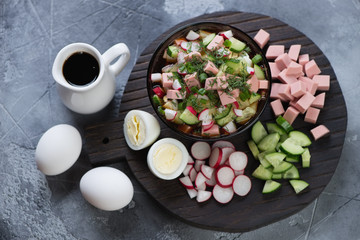 Okroshka or cold soup with kvass, sausage and vegetables. High angle view over grey stone background