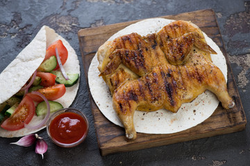 Roasted chicken tabaka with wheat wraps and fresh vegetables on a brown stone background, studio shot