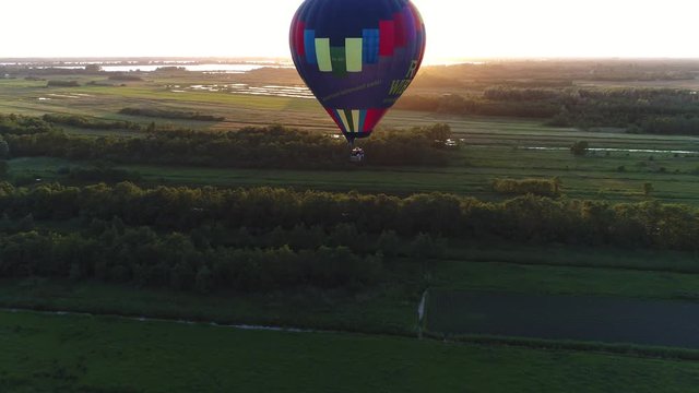 Aerial bird view near hot air ballon moving up during sundown aircraft moving to left over nature reserve meadows and pastures in far background warm colors of sundown sunlight showing on horizon 4k