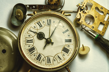 A retro clock from the past disassembled into gears. Tweezers mechanic in the foreground