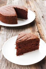 Sliced homemade chocolate cake on white plate over wooden table.