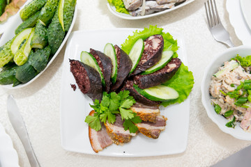 Sausage krovyanka, cut into pieces with fresh cucumber and greens close-up.