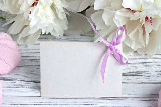 White peonies flowers with empty greeting card on a white wooden background - stock image.