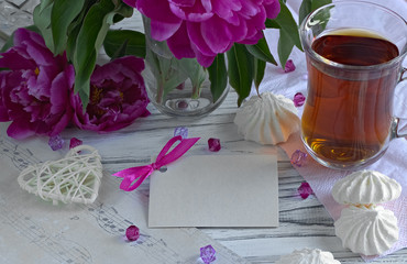 Peonies flowers pink glass of tea with greeting card marshmallow on a white wooden background - stock image.