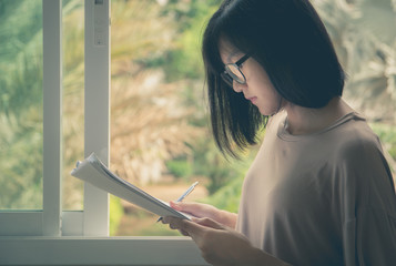 woman wearing glasses sitting and holding paper sheet and reading an exam
