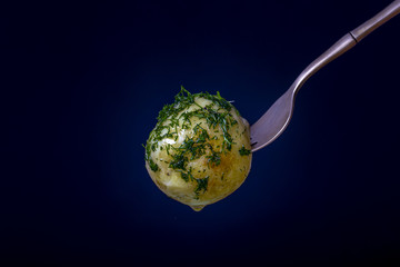 Fork with boiled young potato on a black background. Close up