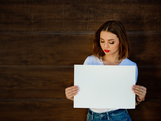 Sad young girl, holding empty sign board. Wooden background.