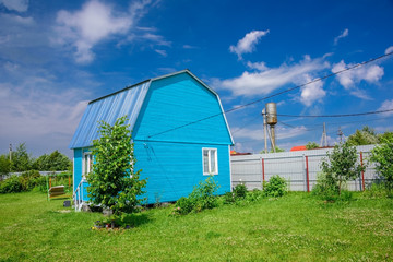 Bright blue summer house, fence and electrical wires on a background of blue sky with white clouds at summer sunny day in countryside