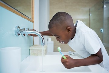 Side view of boy spitting while holding brush in sink