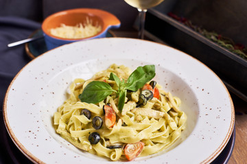 Pasta with chicken, olives and cheese on ceramic plate with glass of white wine