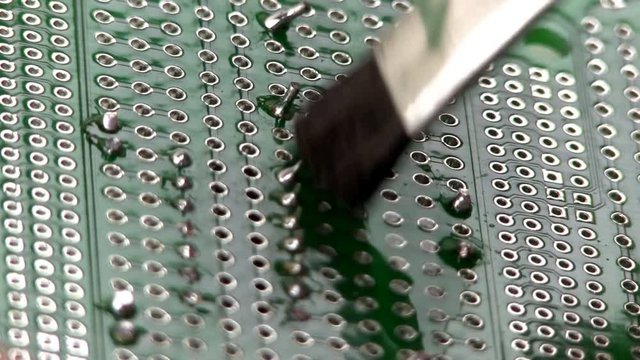 An electrical engineer builds a circuit design by cleaning excess flux and residue after soldering through hole components to a breadboard by hand