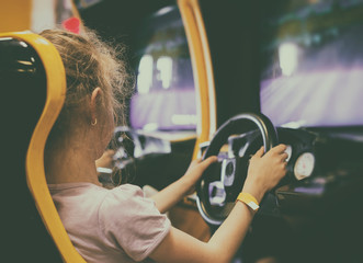 Little girl playing racing simulator game in theme park.