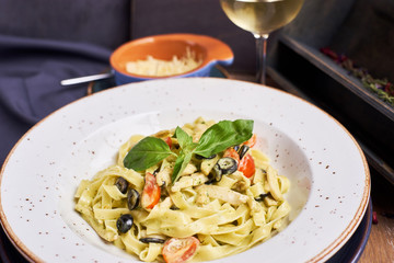 Pasta with chicken, olives and cheese on ceramic plate with glass of white wine
