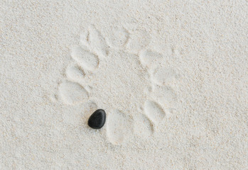 Fototapeta na wymiar black stone on white sand background with stone footprint